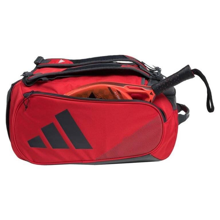 Eine Adidas Tour 3.3 Solar Rot Padeltasche mit schwarzen Akzenten und einem auffälligen schwarzen Logo an der Seite wird ausgestellt. Die Tasche ist leicht geöffnet und zeigt im Inneren einen orangefarbenen Tennisschläger, während ein Tragegurt und ein Reißverschluss ihre Funktionalität verbessern.