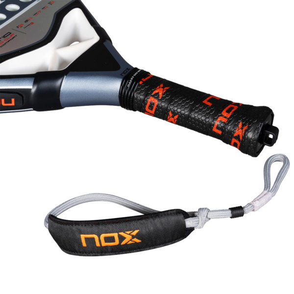 Eine Nahaufnahme des NOX AT10 Pro Cup Comfort 2025 Padelschlägergriffs zeigt einen schwarz-orangefarbenen Griff, der die Marke „Nox“ zeigt. Die abnehmbare Handschlaufe, die mit einem gepolsterten schwarzen Stück mit dem „Nox“-Logo verziert ist, ergänzt das metallisch-schwarze Design wunderbar.