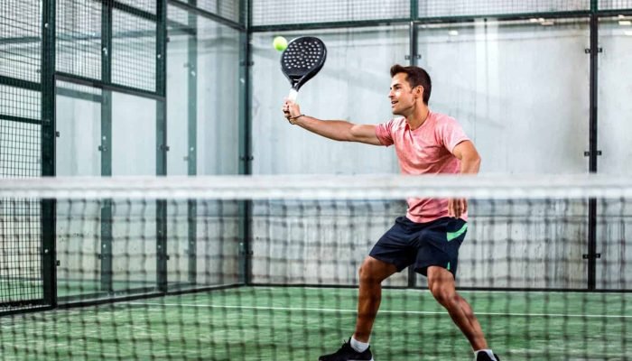 Man playing padel in a green grass padel court indoor behind the net